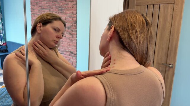 Woman looking in the mirror and examining a skin rash with red inflamed dots on the side of her neck