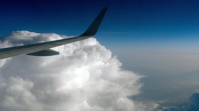 Airplane wing flying above thick white cumulus clouds during high altitude flight, bright daylight, steady window POV shot.