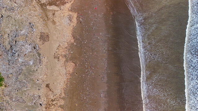 Aerial view of plastic trash and debris scattered along the sandy coastline, highlighting the environmental pollution problem on a beach in Indonesia.