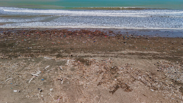 Aerial view of plastic waste and debris scattered across the sandy beach shoreline in Indonesia.