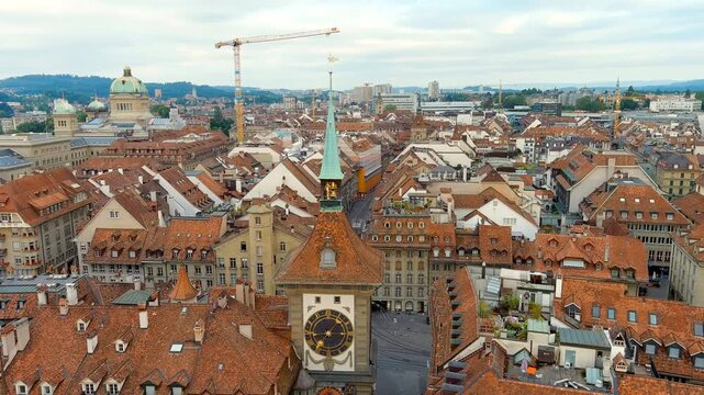 Bern, Switzerland. The Zytglogge medieval clock tower, steep copper spire and astronomical dial rising above terracotta rooftops, aerial panoramic view over the Old Town on a summer morning. Drone fo