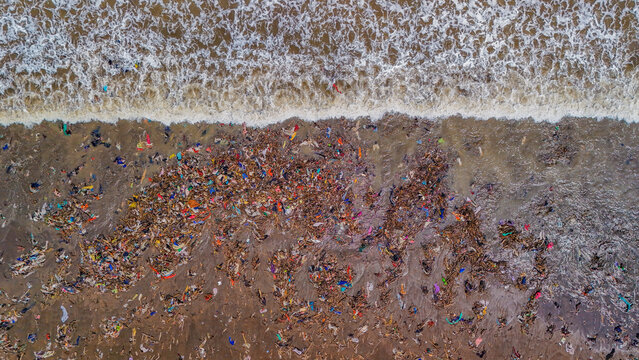 Aerial view of a beach heavily polluted with plastic waste and debris, with ocean waves washing onto the shore in Indonesia.
