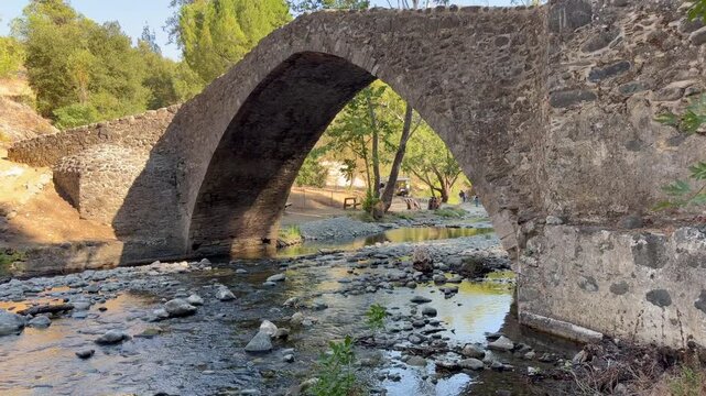 Troodos, Cyprus - August 2, 2026. Scenic view of Tzelefos Bridge over a rocky river. Historic Venetian architecture blends with forest and mountain landscape. Shallow rocky stream 