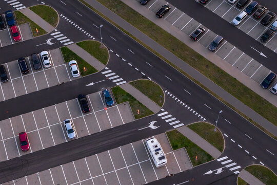 Aerial view of a parking lot with various cars parked in marked spaces, including a white camper van, asphalt lanes with white road markings, and green grass patches in Poland.