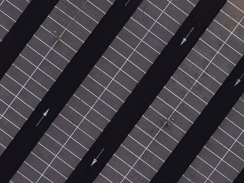 Aerial view of a parking lot with diagonal parking spaces, white lane markings, and directional arrows on the asphalt in Poland.