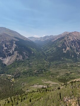 Aerial view of Sheep Gulch Trailhead nestled in a lush mountain valley with dense pine forests and rugged peaks under a clear blue sky in Buena Vista, Colorado, United States.