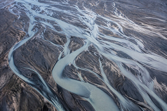 Braided glacial river stream weaving through dark volcanic sediment plains with sediment deposits illustrating natural water path movement for earth study.
