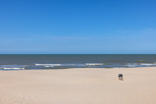 A lone trash can sitting on a vast sandy beach under a clear sky in Middelkerke - Belgium