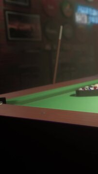 A group of friends is gathered around a green pool table in a dimly lit bar. They take turns aiming and shooting the balls, enjoying the game and each others company.