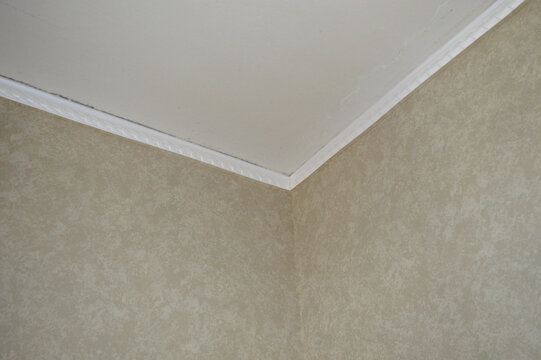 White ceiling crown molding in room corner with beige textured wallpapered walls. Interior apartment finish, home renovation, decorative stucco border, architecture and ceiling repair concept
