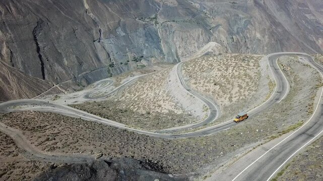 Scenic aerial view: Yellow school bus camper traveling  acrosss Peru&rsquo;s winding roads with arid mountains background.