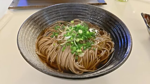 Bowl of soba buckwheat noodles in katsuobushi dashi broth, Japanese Food Cuisine, Healthy Meal, Scallion Garnish, Rotating Shot