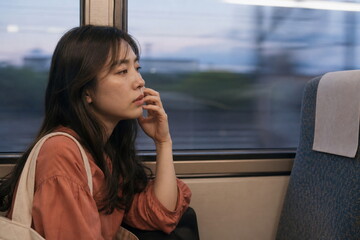 Fototapeta premium 夕方の電車内で頬に触れる女性の横顔
