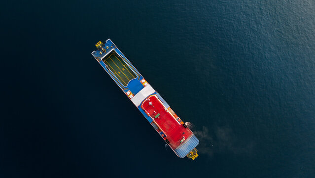 Aerial view of a ferry boat navigating the deep blue waters near Ketapang Ferry Port, showcasing its red deck and vehicle loading area in Banyuwangi, East Java, Indonesia.