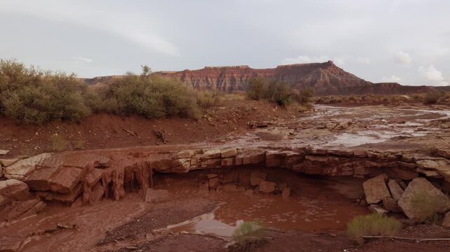 Muddy water pours over a sandstone ledge in a shallow ravine in the desert below Gooseberry Mesa, Utah USA after heavy rains have passed, the day fades to evening and the clouds begin to break up.