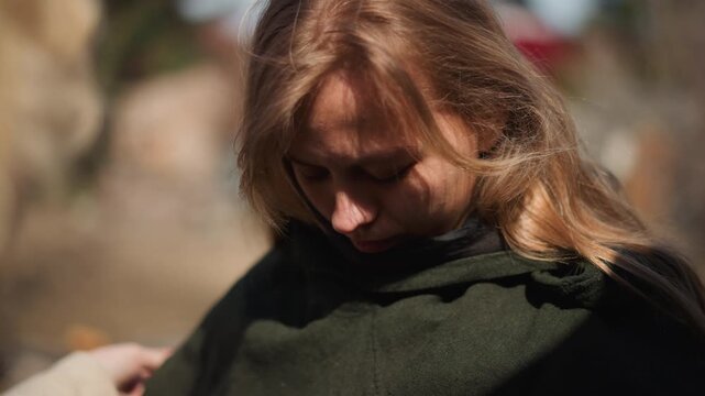 A woman adjusts her clothing while looking down and then up, creating a contemplative moment in an outdoor environment. The scene is captured in a close-up, focusing on her upper body.