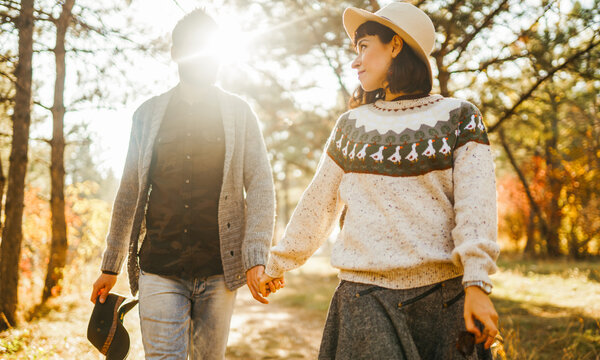 A loving couple spends time together in a sunny forest. A young woman and man, dressed stylishly, stroll and relax on an autumn day at sunset. The concept of love, relaxation, and enjoyment.