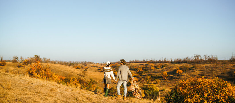 A loving couple spends time together in a sunny forest. A young woman and man, dressed stylishly, stroll and relax on an autumn day at sunset. The concept of love, relaxation, and enjoyment.