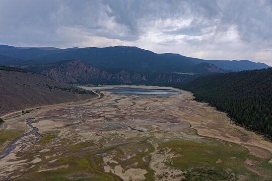 Aerial view of Clear Creek Reservoir with low water levels surrounded by mountains, pine forests, and dry landscape in Chaffee County, Colorado, United States.