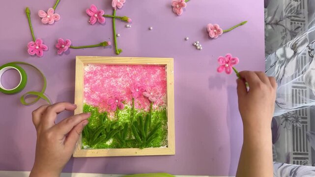 POV view of a child hands bending pink chenille stem making a flower petal for a DIY kids crafts school project inside a bright creative workshop