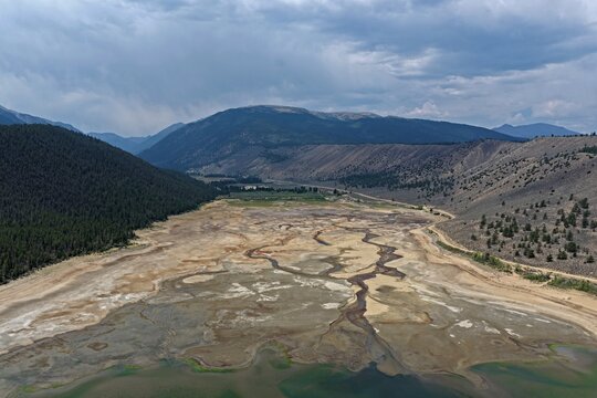 Aerial view of Clear Creek Reservoir showing low water levels with exposed mudflats and winding channels surrounded by mountains in Chaffee County, Colorado, United States.