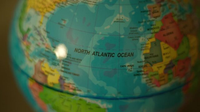 Globe spins slowly, showing North Atlantic Ocean. Colorful continents and oceans clearly labeled. Close-up view emphasizes educational or travel theme. Ideal for geography, education.