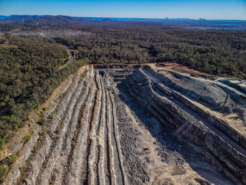 Aerial view of Holcim Australia - Petrie Quarry showing terraced rock walls and mining pits surrounded by dense forest in Kurwongbah, Queensland, Australia.