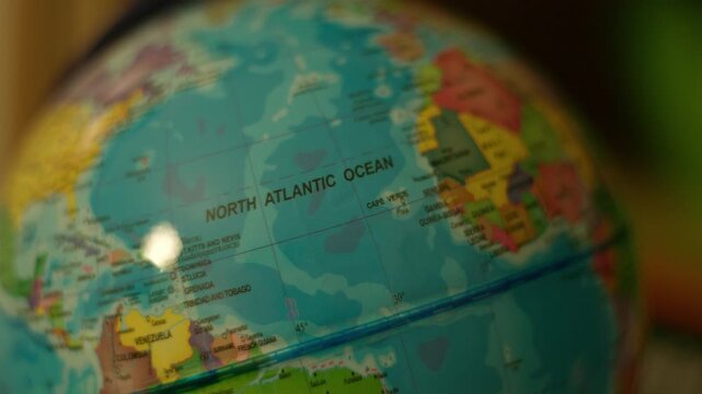 Close-up globe highlights North Atlantic Ocean. Colorful map shows continents and ocean with clear labels. Focus stays sharp on ocean area, blurring surrounding landmasses. Ideal for educational