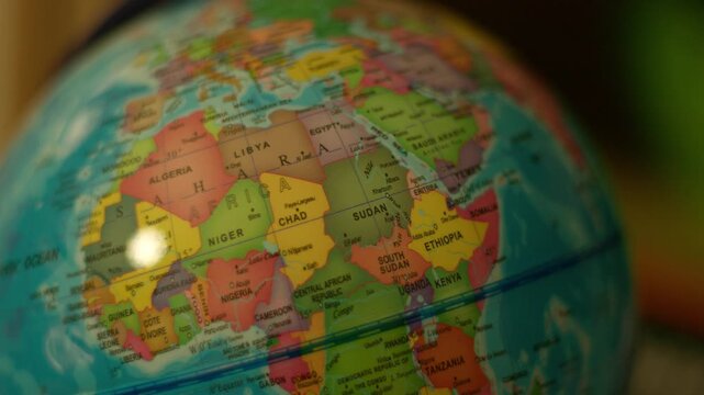 Colorful globe rotates slowly, showing continents. Bright lights reflect off its curved surface. Close-up emphasizes detail and texture. Ideal for educational or travel-themed projects