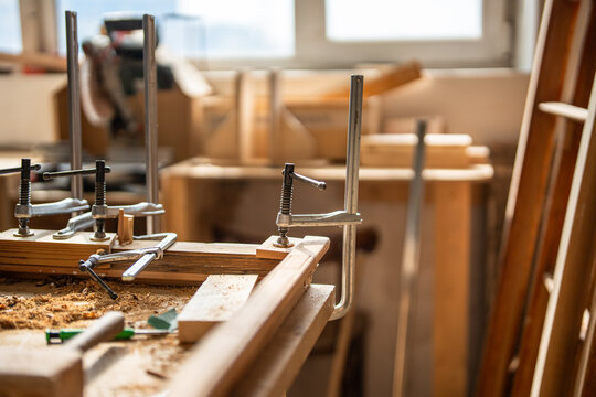 Antique wooden frame repair in woodworking studio, window frame fixed to workbench with clamp tools, restoration workshop workstation with wooden boards gluing under strong fixation using instruments.