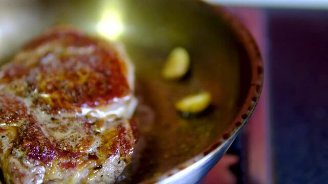 A beef steak cooks over high heat while butter becomes dark and garlic browns in the pan. Light smoke rises, showing an overheated cooking process before serving.