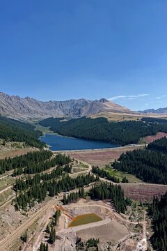 Aerial view of Clinton Gulch Dam Reservoir surrounded by dense pine forests and rugged mountains under a clear blue sky in Summit County, Colorado, United States.