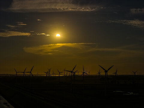 Aerial view of wind turbines silhouetted against a dramatic sunset sky with golden light reflecting over the landscape in Emden, Niedersachsen, Germany.