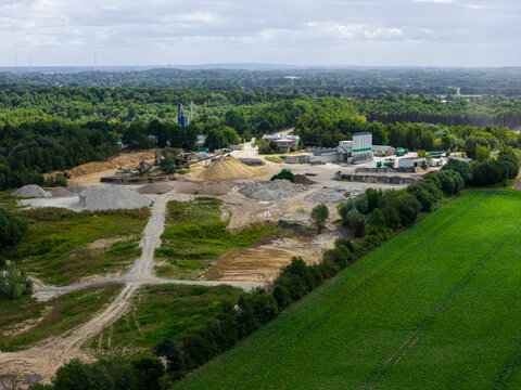 Aerial view of an industrial sand and gravel extraction site with piles of aggregate, processing machinery, and surrounding green fields in Konin, Wielkopolskie, Poland.