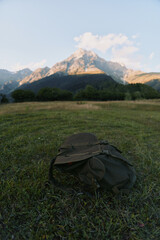 Naklejka premium Backpack resting on a sunlit field with distant mountain range, evoking outdoor adventure, hiking, and travel lifestyle in a calm nature scene with expansive landscape.