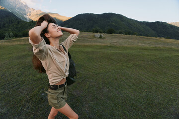 Fototapeta premium Woman enjoying outdoor life, standing in a meadow with arms raised, smiling, backpack visible. Nature mood, wellness, and freedom in a sunny landscape.
