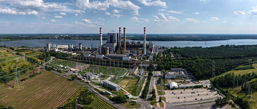 Aerial view of the ZE PAK S.A. Patnow Power Plant situated on the shore of a large lake, surrounded by green forests, power lines, and agricultural fields in Konin, Wielkopolskie, Poland.