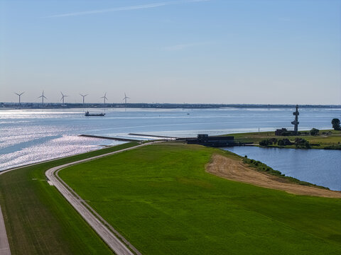 Aerial view of the coastal landscape near the Volkswagenwerk Emden, featuring green fields, a road, wind turbines, and a cargo ship on the water in Emden, Niedersachsen, Germany.