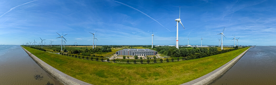 Aerial view of the Volkswagenwerk Emden industrial facility surrounded by wind turbines and green fields along the coastline in Emden, Niedersachsen, Germany.