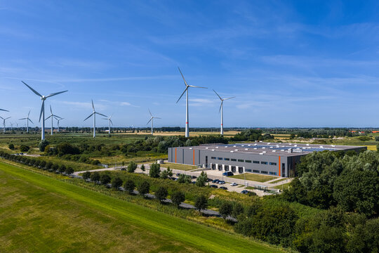 Aerial view of the Volkswagenwerk Emden factory complex surrounded by wind turbines and green fields under a clear blue sky in Emden, Niedersachsen, Germany.