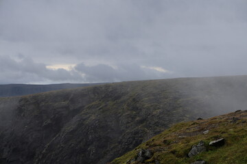 Steep dark rocky cliffs of Nordkapp partially veiled in light mist under overcast arctic skies. © Adam