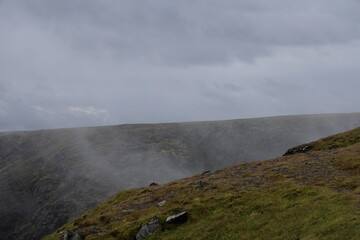 Steep dark rocky cliffs of Nordkapp partially veiled in light mist under overcast arctic skies. © Adam
