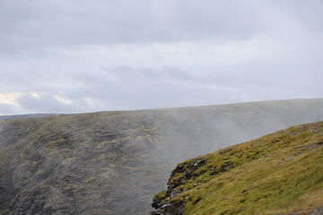 Misty arctic mountain landscape at Nordkap, with rocky cliffs and fog rolling over grassy tundra under an overcast sky. © Adam