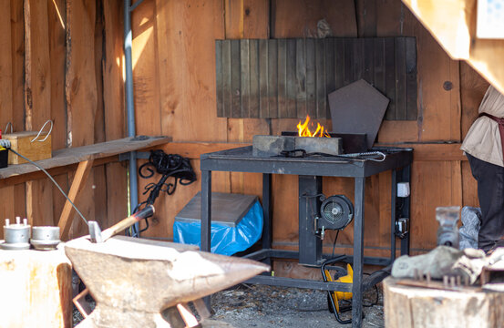 Blacksmith workshop interior shows an anvil, a forge with flames, and various tools on a workbench in a rustic wooden environment