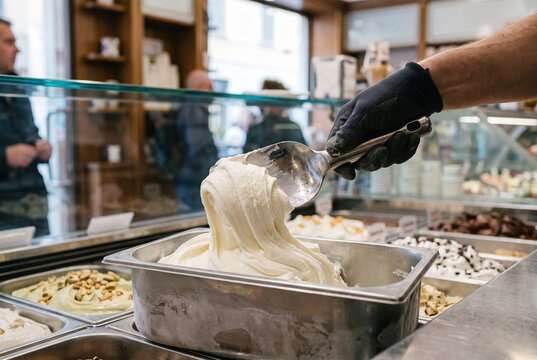 Worker hand scooping creamy white Italian gelato with metal spade in authentic gelateria