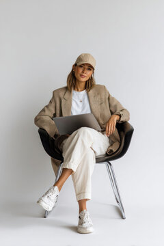 A photo of a woman sitting in the black chrome chair with her legs crossed and holding laptop on lap blazer electronics fashionable.