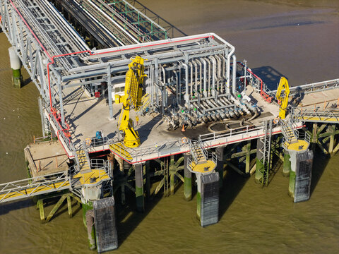 Industrial Oil Terminal Pier With Yellow Loading Arms Located on the River by Day