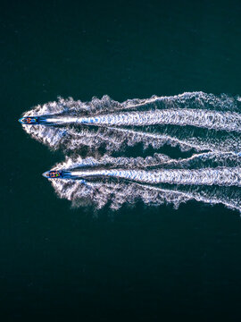 Aerial view of two jet skis speeding across dark blue water, leaving long white wakes behind them in Cascais, Lisbon, Portugal.