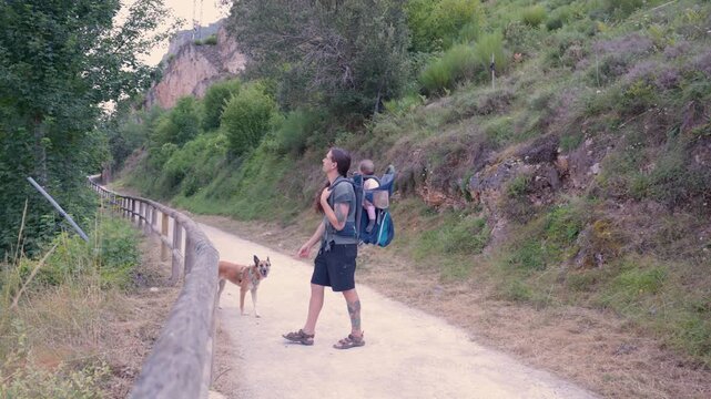 Father carrying baby in backpack carrier hiking with dog