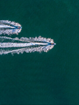 Aerial view of two jet skis speeding across the deep blue sea, leaving long white wakes behind them in Cascais, Lisbon, Portugal.